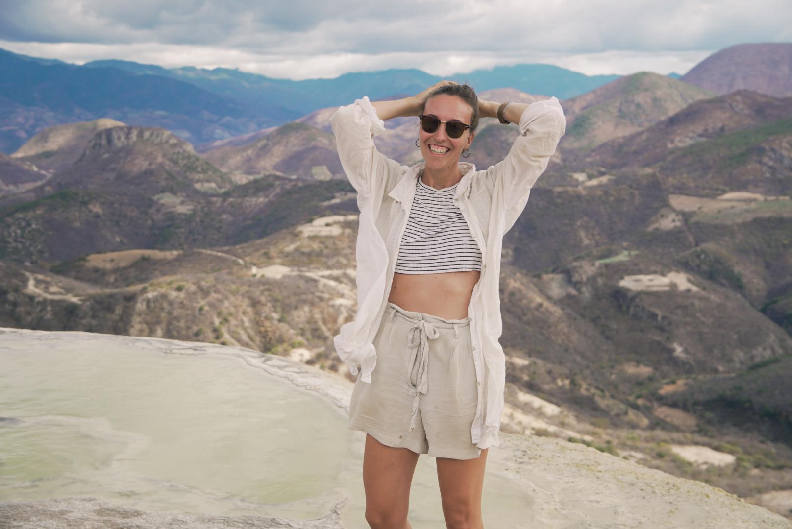 Lachende junge Frau, die sich in die Haare greift vor einer hügeligen Landschaft.