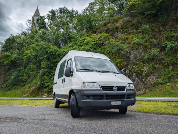 Weisser Fiat Ducato Camper vor grünen Bäumen.
