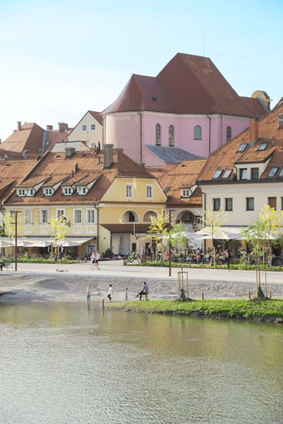 Fussgängerzone am Fluss in Maribor mit bunten Häusern im Hitnergrund.