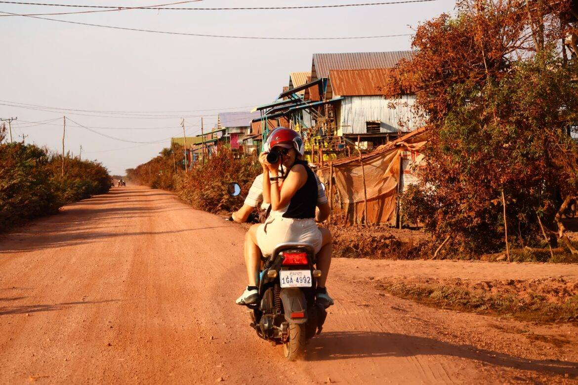 Frau die auf einem Roller sitzt und mit einer Kamera Fotos schiesst.